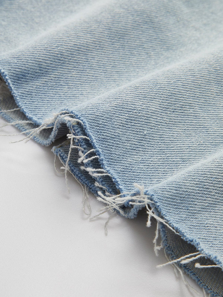 Zoom sur l'ourlet effiloché de la veste en jean courte Clementine. Ce détail déstructuré ajoute une touche de style moderne et décontracté, mettant en valeur le look tendance et contemporain de la veste. Le tissu en denim bleu clair est à la fois doux et légèrement texturé, parfait pour un look casual chic.