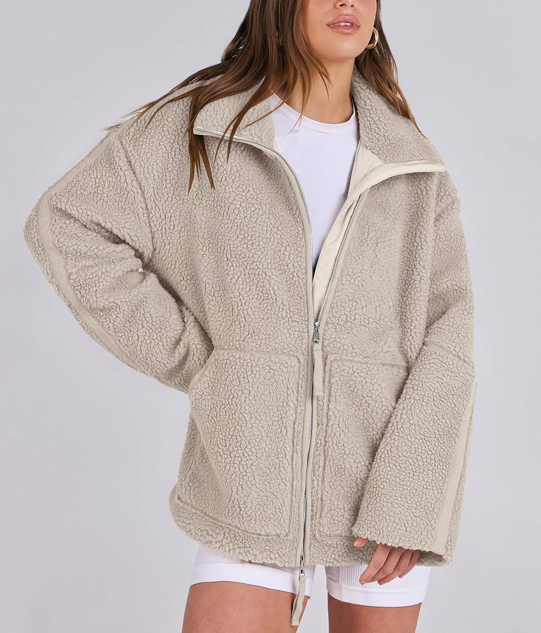 Veste en tissu peluche beige clair pour femme, douce et confortable au toucher. Ce modèle présente une fermeture éclair argentée à l’avant, un col montant et deux grandes poches frontales. Sa coupe oversize et son style moderne en font un vêtement idéal pour un look décontracté et tendance pendant les journées fraîches d’automne et d’hiver.