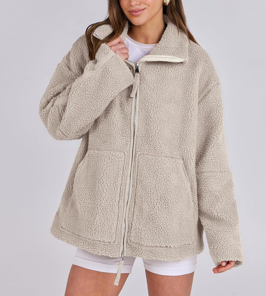 Veste en tissu peluche beige clair pour femme, douce et chaude au toucher. Ce modèle présente une fermeture éclair argentée à l’avant, un col montant et deux grandes poches plaquées. Son design oversize et décontracté offre un style moderne et confortable, parfait pour les journées fraîches d’automne et d’hiver.