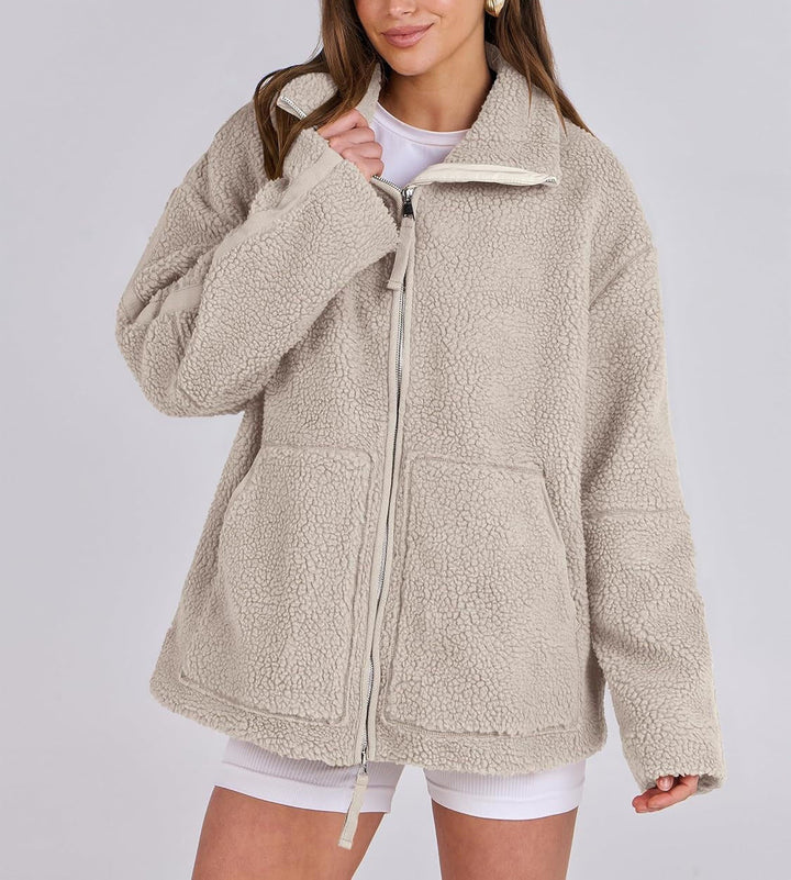 Veste en tissu peluche beige clair pour femme, douce et chaude au toucher. Ce modèle présente une fermeture éclair argentée à l’avant, un col montant et deux grandes poches plaquées. Son design oversize et décontracté offre un style moderne et confortable, parfait pour les journées fraîches d’automne et d’hiver.