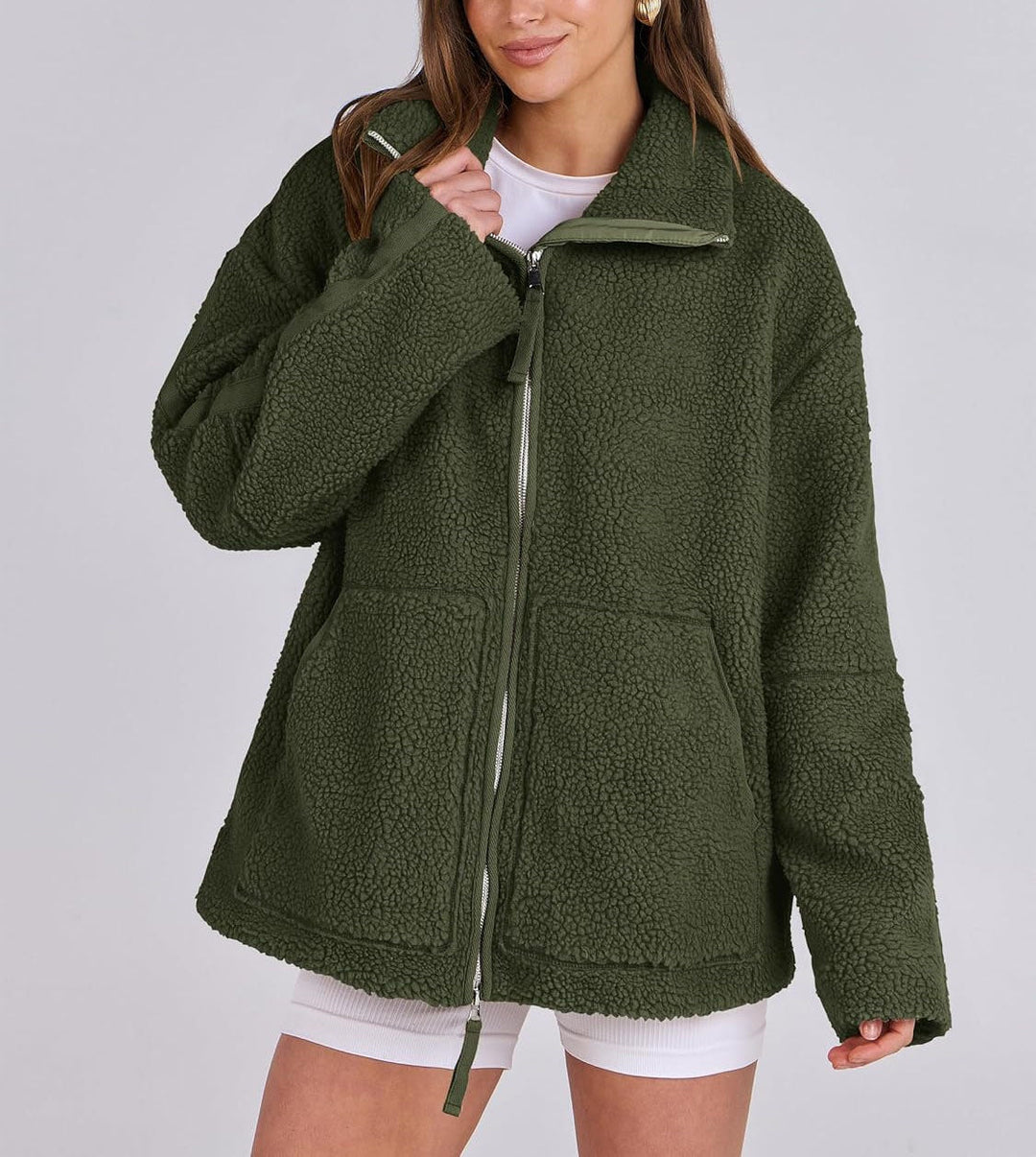 Veste en peluche verte pour femme, douce et chaude au toucher. Ce modèle est doté d'une fermeture éclair argentée sur le devant, d'un col montant et de deux grandes poches plaquées. Sa coupe ample et décontractée offre un look moderne et confortable, idéal pour les fraîches journées d'automne et d'hiver.