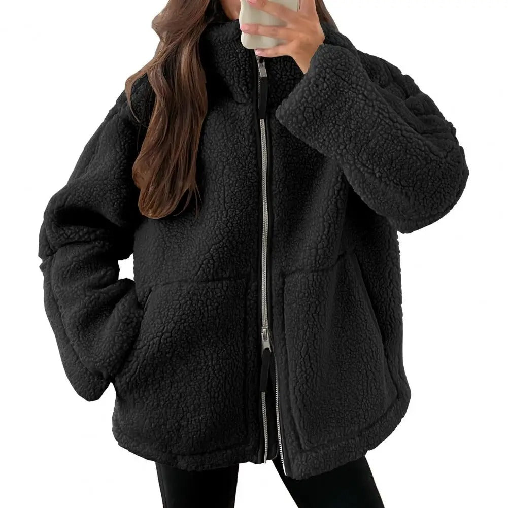 Veste en tissu peluche noire pour femme, à la texture douce et épaisse. Ce modèle présente une fermeture éclair argentée à l’avant, un col montant et deux grandes poches plaquées. Son style oversize et moderne offre un look à la fois confortable et tendance, idéal pour les journées fraîches d’automne et d’hiver.