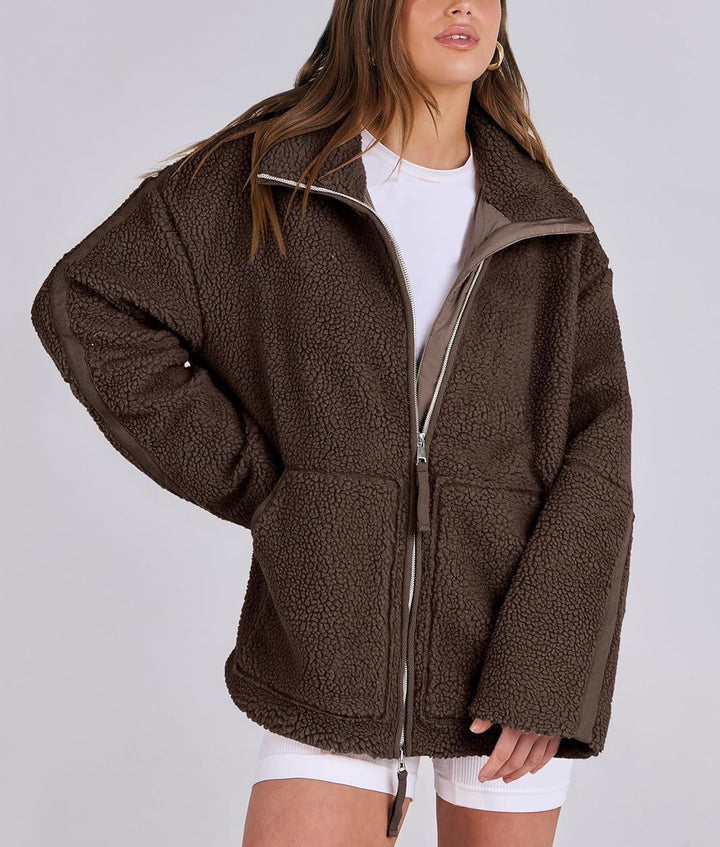 Veste en tissu peluche marron foncé pour femme, douce et confortable au toucher. Ce modèle présente une fermeture éclair argentée à l’avant, un col montant et deux grandes poches plaquées. Son style oversize et décontracté apporte une touche moderne et cosy, parfaite pour les journées fraîches d’automne et d’hiver.