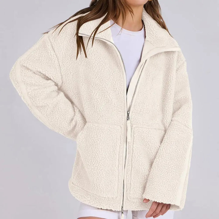 Veste en tissu peluche blanc cassé pour femme, à la texture douce et confortable. Ce modèle présente une fermeture éclair à l’avant, un col montant et deux grandes poches latérales. Son style décontracté et tendance en fait un choix idéal pour les journées fraîches ou les tenues casual d’automne et d’hiver.