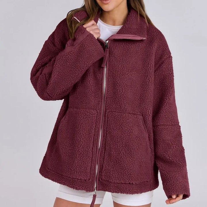 Veste rouge en peluche pour femme, douce et moelleuse. Ce modèle est doté d'une fermeture éclair sur le devant, d'un col montant et de deux grandes poches plaquées. Un style à la fois décontracté et moderne, idéal pour les journées fraîches ou pour composer des tenues d'automne et d'hiver à la fois confortables et élégantes.