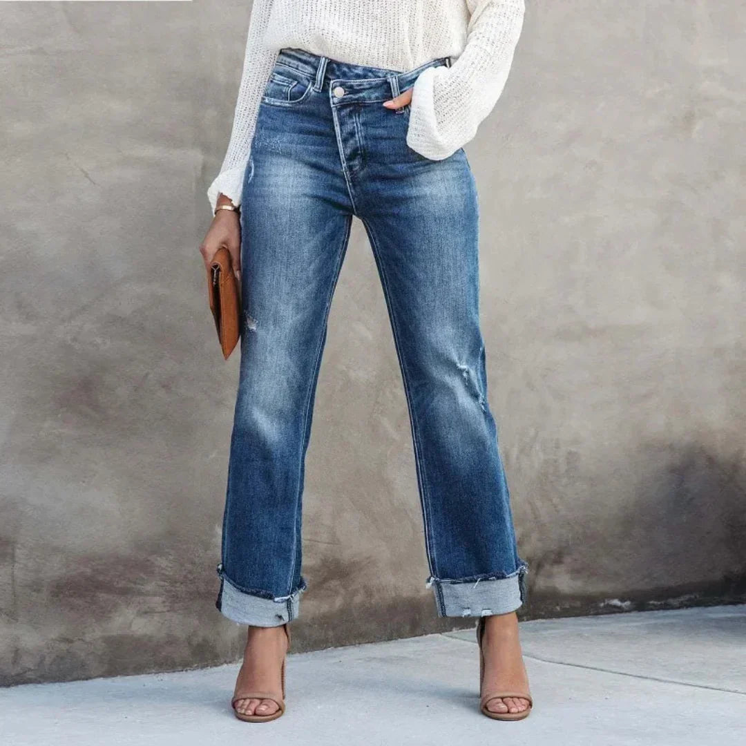 Pantalon droit femme Delia moderne en jean bleu, taille haute avec ourlet retroussé, porté avec un pull blanc et des sandales à talons.