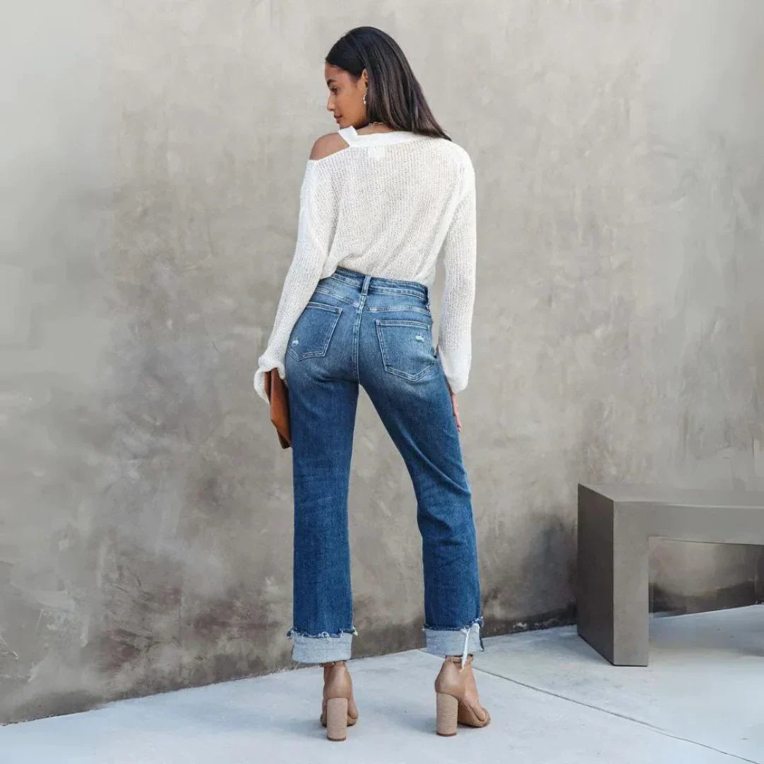 Vue de dos du pantalon droit femme Delia moderne en jean bleu, taille haute avec poches arrière et ourlets retroussés, porté avec un pull blanc et des sandales à talons.