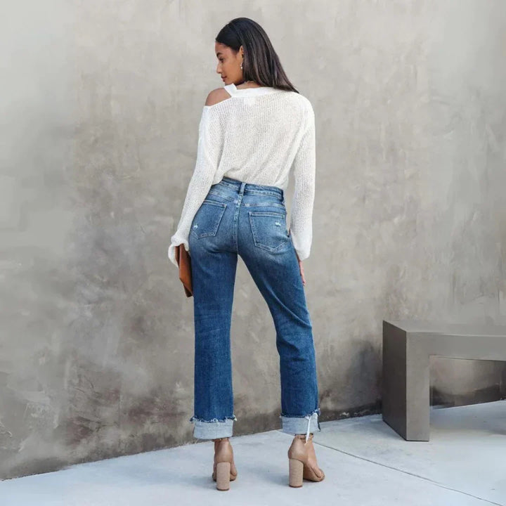 Vue de dos du pantalon droit femme Delia moderne en jean bleu, taille haute avec poches arrière et ourlets retroussés, porté avec un pull blanc et des sandales à talons.