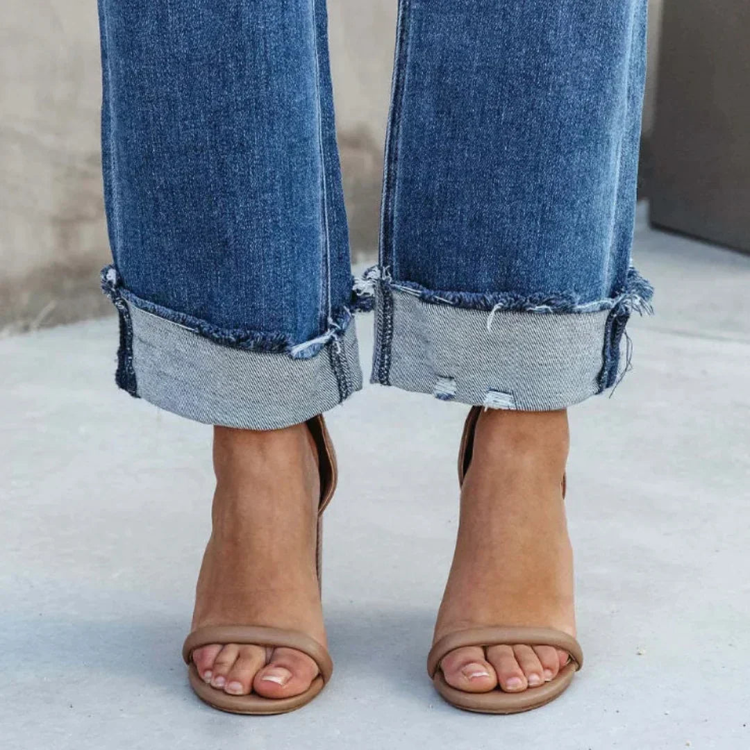 Gros plan sur le pantalon droit femme Delia moderne en jean bleu, bas de jambe avec ourlets retroussés et bords effilochés, porté avec des sandales à talons.