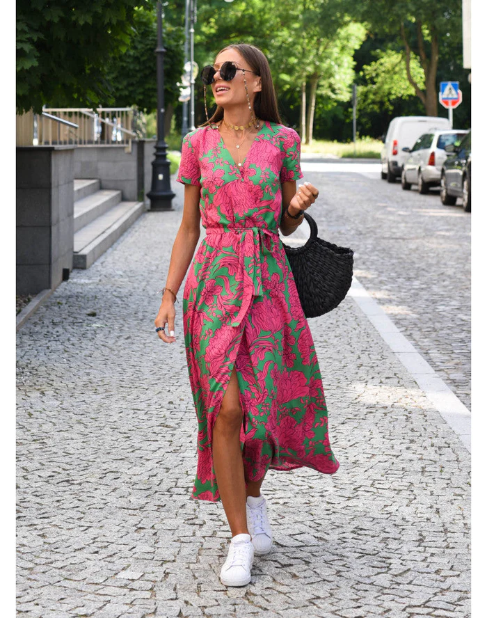 Robe midi femme Demi au style moderne, avec col en V et imprimé floral rose et vert. Coupe fluide avec ceinture à la taille, portée avec des baskets blanches et un sac noir pour un look estival chic et décontracté.