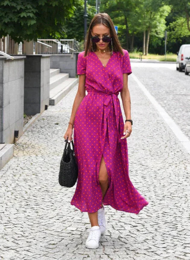 Robe midi femme Demi au style moderne avec col en V et motif à pois sur fond rose. Coupe fluide avec taille cintrée et lien à nouer, offrant une silhouette élégante, idéale pour un look estival chic et décontracté.