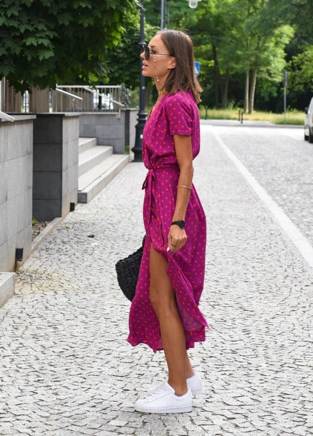 "Vue de profil de la robe midi femme Demi au style moderne, avec col en V et motif à pois sur fond rose. Coupe fluide avec taille cintrée et lien à nouer, mettant en valeur une silhouette élégante pour un look estival chic et décontracté.