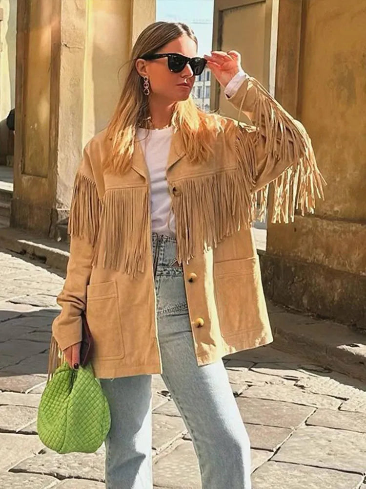 Veste à franges pour femme, modèle Domitille. Veste beige en suède avec franges sur les manches et le devant, portée avec un t-shirt blanc et un jean taille haute. Complétée par un sac vert vif, un look tendance et dynamique pour un style moderne.