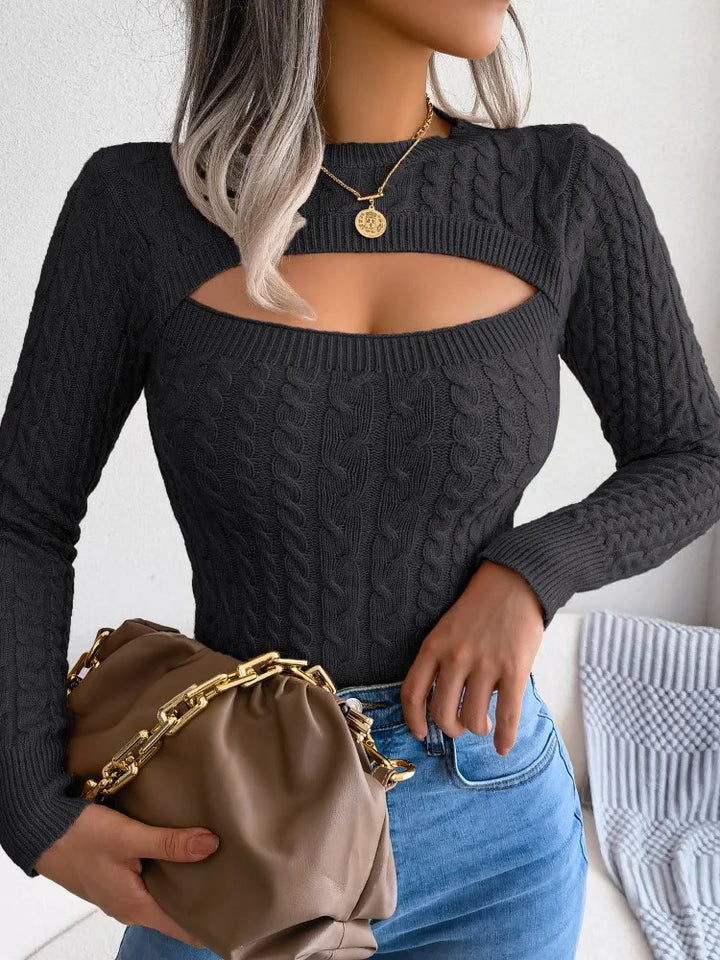 Haut tricoté à manches longues pour femme, couleur noire, avec un décolleté découpé moderne et une texture en tricot torsadé. Le modèle est porté avec un jean bleu et un sac à main beige à chaîne dorée, créant un look tendance et élégant pour une allure décontractée chic.