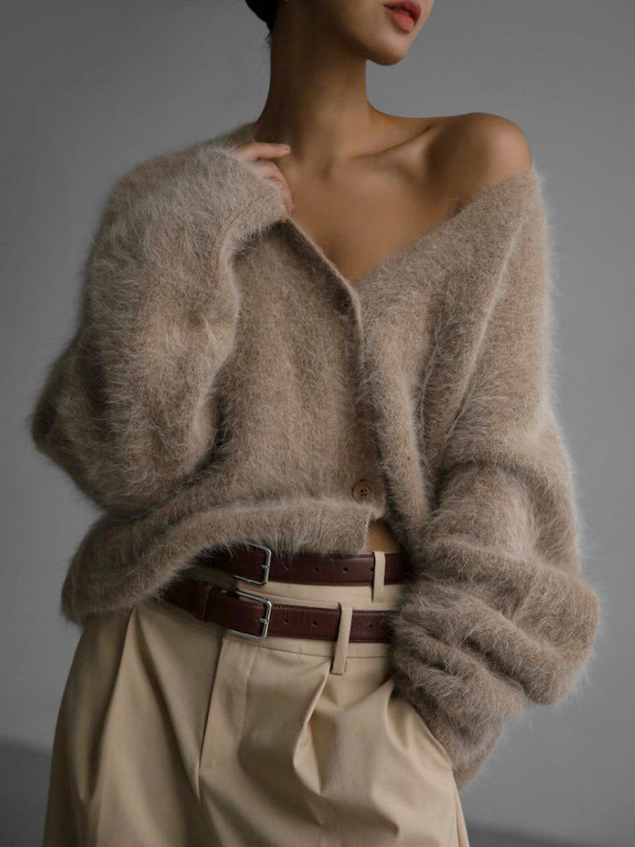 Un cardigan en mohair doux, de couleur beige clair, porté avec un pantalon beige et une ceinture en cuir marron. Le cardigan est légèrement ouvert sur le devant, créant un look décontracté et élégant.