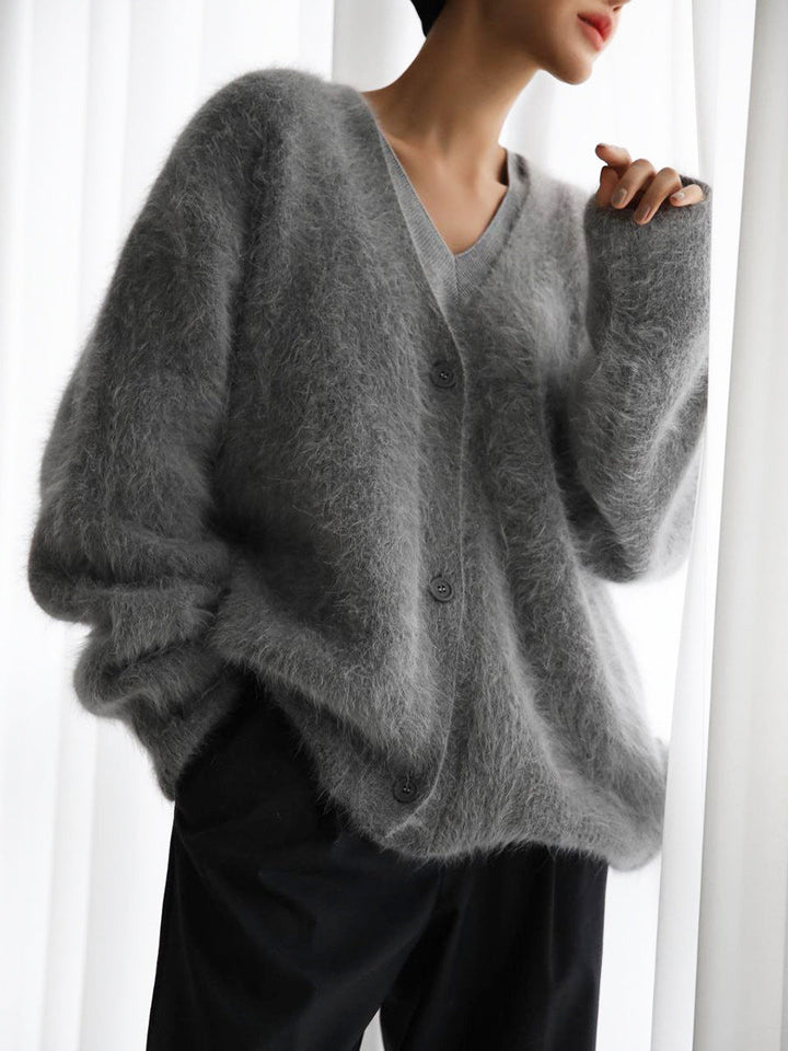 Un cardigan en mohair doux de couleur grise, avec une coupe ample et des boutons sur le devant. Il est porté sur une tenue décontractée, apportant confort et élégance à l'ensemble.