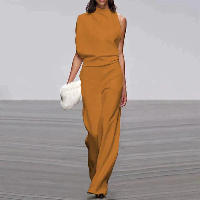 Abette | Combinaison chic pour femme, élégante et moderne, de couleur moutarde avec une coupe asymétrique et un pantalon à large jambe, parfait pour une soirée, accompagnée d'un sac à main en fourrure.