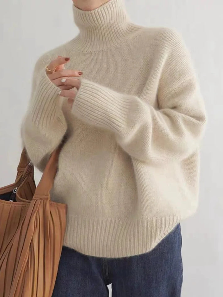 Pull à col roulé femme crème en maille douce et chaude, coupe oversize avec poignets et ourlet côtelés, porté avec un jean et un sac à franges — parfait pour l’hiver.