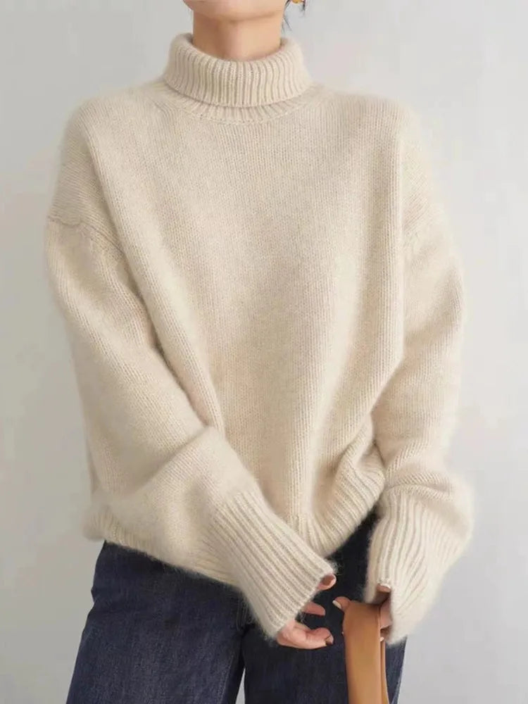 Pull femme à col roulé couleur crème, maille douce et épaisse, coupe ample et manches longues côtelées, porté avec un jean — idéal pour l’hiver.