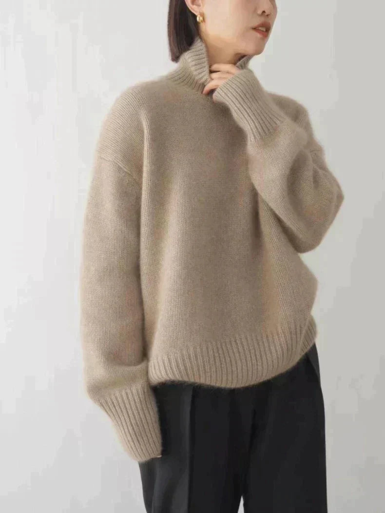 Pull à col roulé femme Éléonore beige taupe en maille douce et chaude, coupe ample avec col montant et finitions côtelées, porté avec un pantalon noir — parfait pour l’hiver.