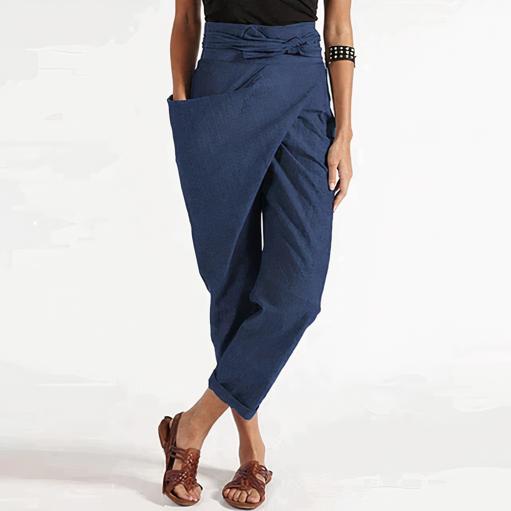 Pantalon d’été bleu marine coupe ample style portefeuille, taille haute nouée avec grand rabat et poches, chevilles retroussées, porté avec sandales marron.