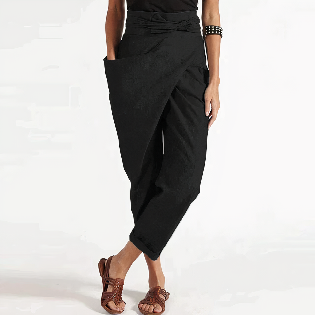 Pantalon d’été noir coupe ample style portefeuille, taille haute nouée avec grand rabat et poches, chevilles retroussées, porté avec sandales marron.