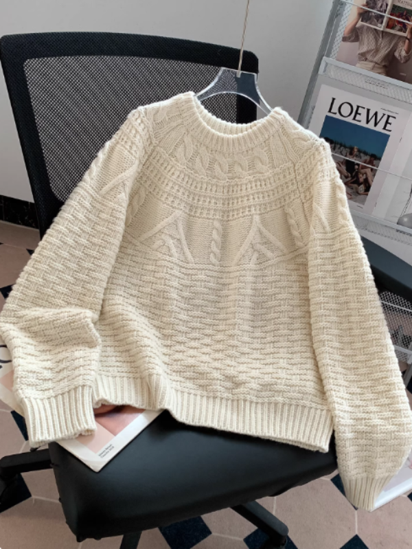 Un gros pull en maille blanche, à col rond et à motifs texturés, est posé sur une chaise de bureau dans un intérieur moderne.