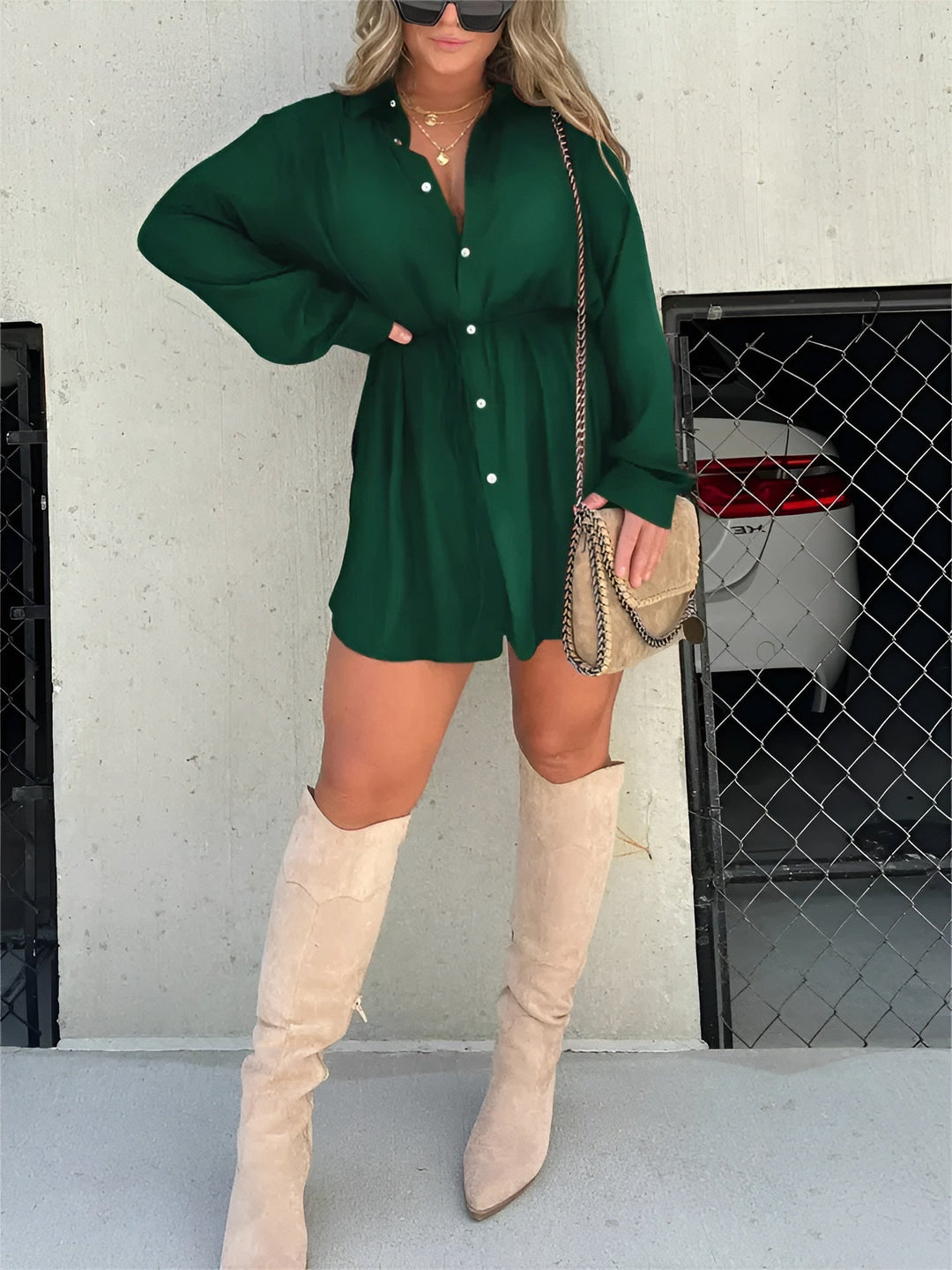 Cette chemise fluide de couleur vert émeraude, avec des boutons et une ceinture à nouer à la taille, offre une silhouette élégante et décontractée. Elle est portée avec des bottes hautes beiges et un sac à bandoulière, pour un look moderne et chic.
