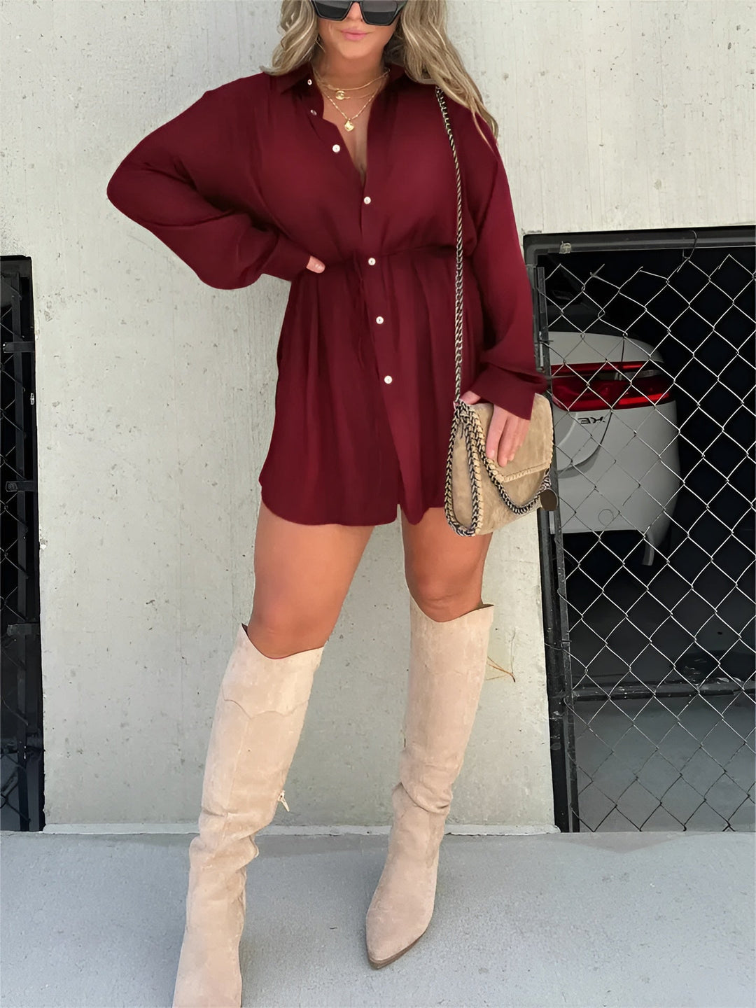 Chemise à manches longues pour femme, modèle tendance. Cette chemise fluide de couleur bordeaux, avec des boutons et une ceinture à nouer à la taille, crée un look élégant et décontracté. Elle est portée avec des bottes hautes beiges et un sac à bandoulière, parfait pour un style moderne et chic.