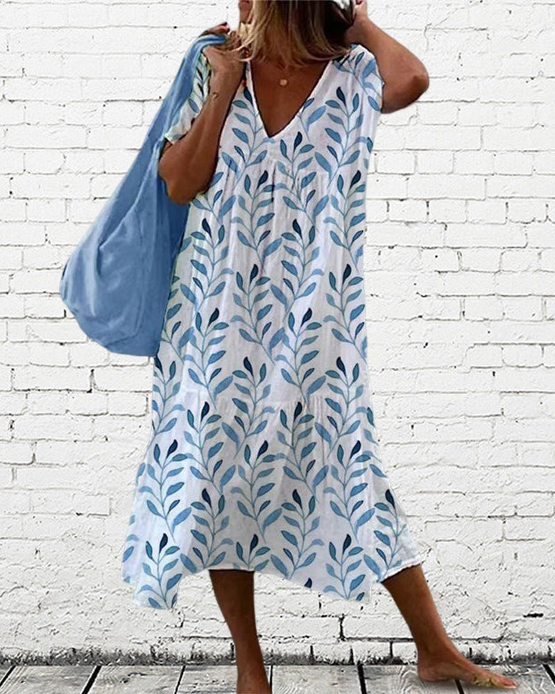 Robe col V Elysia pour femme, coupe ample tendance avec imprimé feuillage bleu sur fond blanc, portée en extérieur avec un sac bleu, style décontracté.