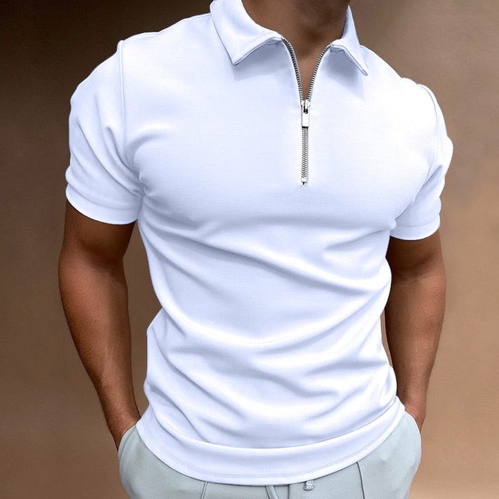 Polo pour homme blanc à manches courtes, coupe ajustée et moderne, doté d’un col avec fermeture zippée, porté avec un pantalon clair pour un style élégant, minimaliste et contemporain.