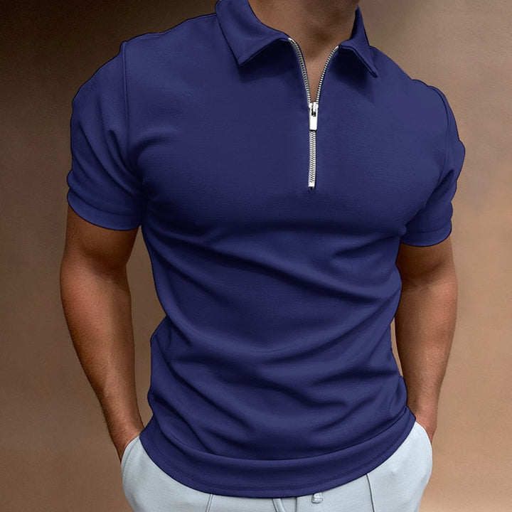 Polo pour homme bleu foncé à manches courtes, coupe ajustée et contemporaine, avec col structuré et fermeture zippée, porté avec un pantalon clair pour un look élégant et moderne.