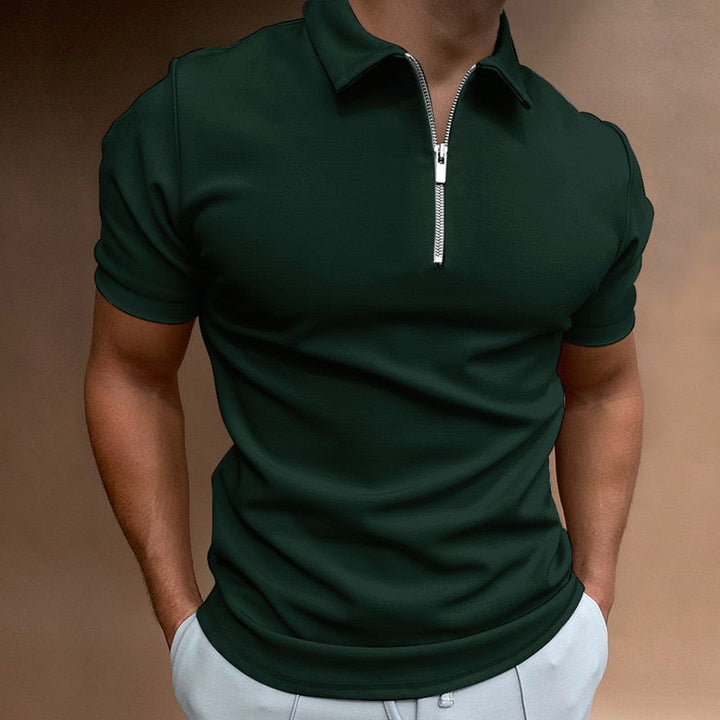 Polo pour homme vert foncé à manches courtes, coupe ajustée et moderne, avec col structuré et fermeture zippée, porté avec un pantalon clair pour un style élégant, raffiné et contemporain.