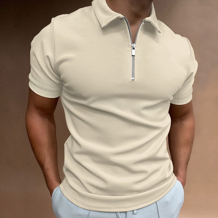 Polo pour homme couleur crème à manches courtes, coupe ajustée et moderne, avec col structuré et fermeture zippée, porté avec un pantalon clair pour un style élégant et contemporain.