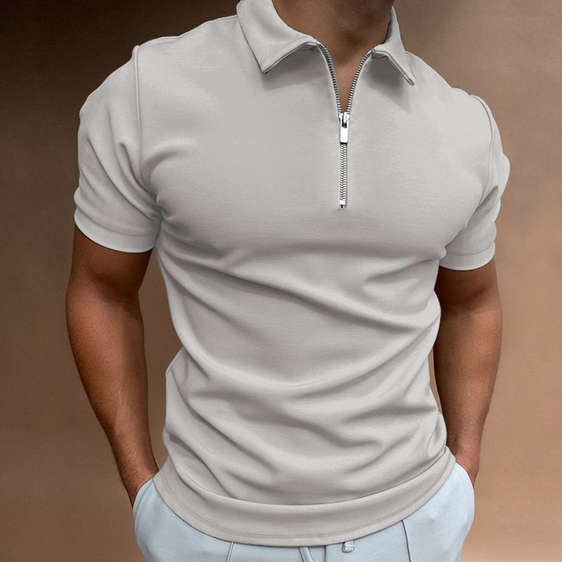 Polo pour homme beige clair à manches courtes, coupe ajustée et contemporaine, avec col structuré et fermeture zippée, porté avec un pantalon clair pour un look élégant, sobre et moderne.