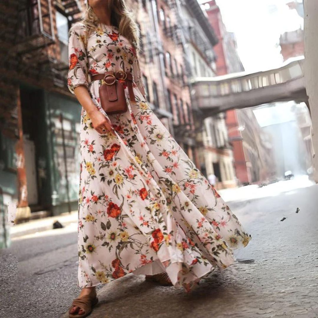 robe blanche fluide à imprimé floral, manches 3/4, taille ceinturée avec sac ceinture, jupe longue évasée en mouvement en milieu urbain.