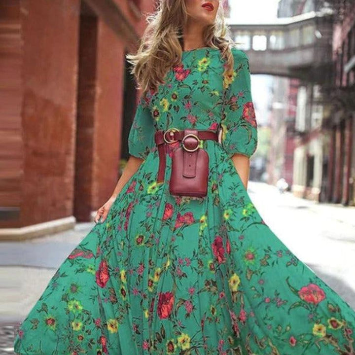 robe verte fluide à imprimé floral multicolore, manches 3/4, taille ceinturée avec sac ceinture, jupe longue évasée en mouvement en ville.