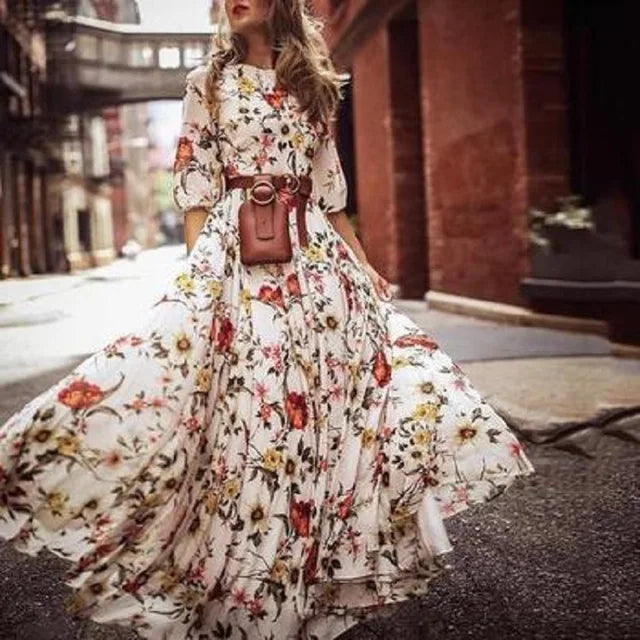 robe blanche à imprimé floral coloré, manches 3/4, taille ceinturée avec sac ceinture, jupe longue très évasée et fluide en mouvement dans une rue urbaine.