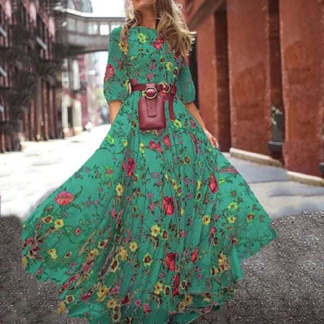 Femme portant la robe maxi longue moderne Estelle  robe verte à imprimé floral multicolore, manches 3/4, taille ceinturée avec sac ceinture, jupe longue très évasée et fluide en mouvement en ville.