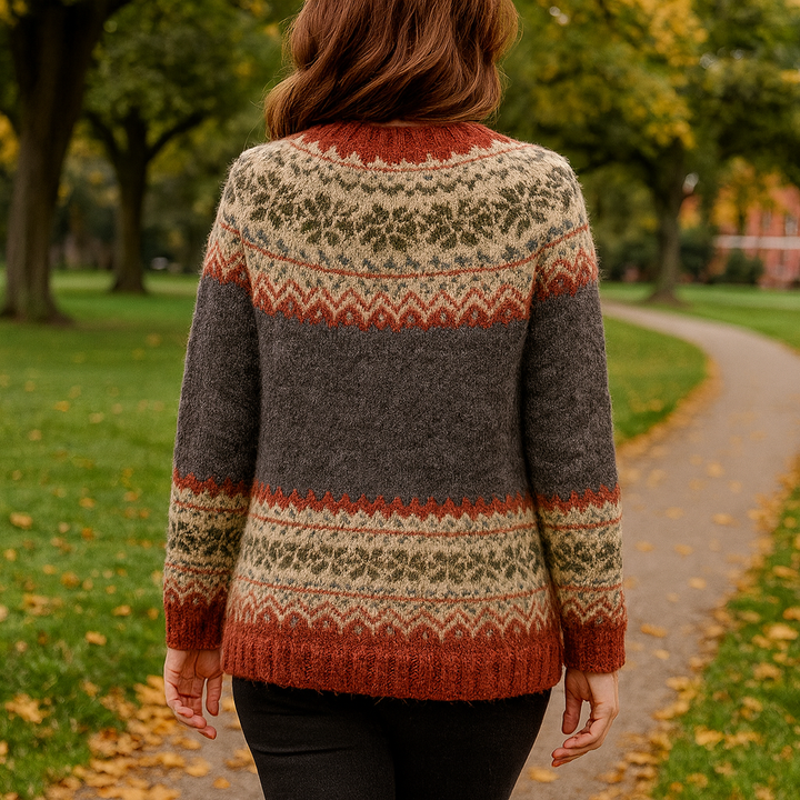 Vue de dos d’une femme portant un cardigan en maille à motif nordique, avec des bandes décoratives en beige, rouge brique et vert sur un fond gris foncé, photographiée en extérieur sur un chemin bordé d’arbres en automne.
