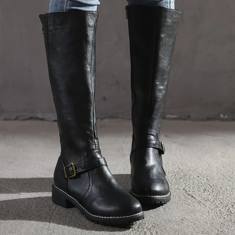 Bottes hautes noires en cuir synthétique pour femme, avec une boucle dorée décorative et une semelle robuste à coutures apparentes. Style classique et raffiné, parfait pour l’hiver, alliant confort et élégance. Portées avec un jean ajusté, elles offrent une allure moderne et intemporelle.