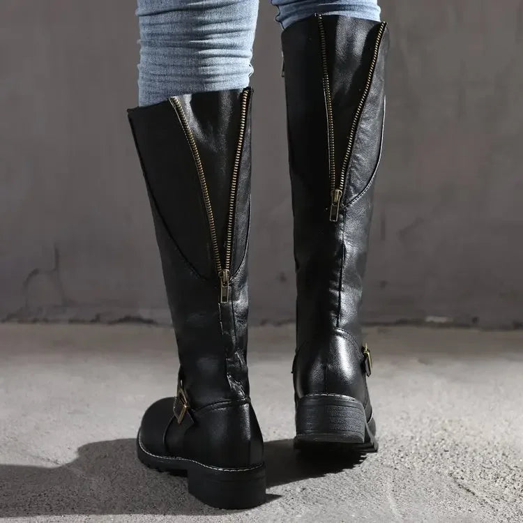 Bottes hautes noires en cuir synthétique pour femme, dotées de fermetures éclair apparentes à l’arrière et de boucles métalliques latérales. Style chic et moderne, offrant confort et durabilité pour la saison hivernale. Portées avec un jean moulant, elles complètent un look élégant et urbain.