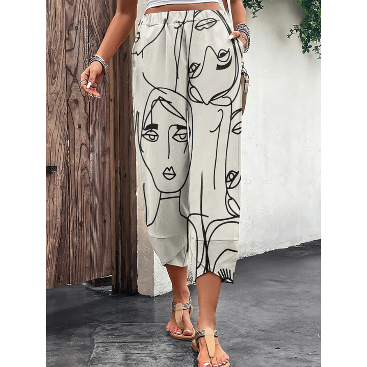 Pantalon ample d’été pour femme, de couleur claire avec imprimé artistique de visages en lignes noires, taille élastique confortable et coupe fluide mi-mollet, porté avec des sandales sur un fond extérieur naturel.