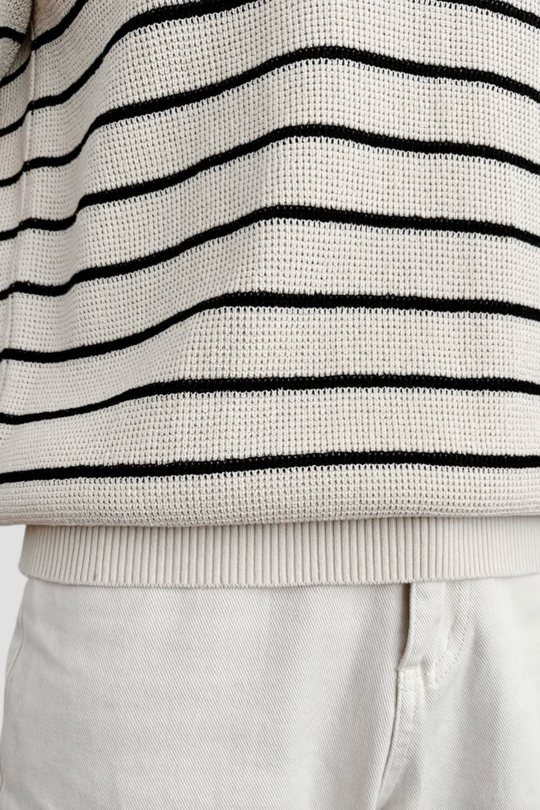 Polo à manches courtes pour homme Felix, tricoté en maille crème avec fines rayures noires horizontales, vue rapprochée sur le bas du vêtement et la taille, style tendance et moderne.