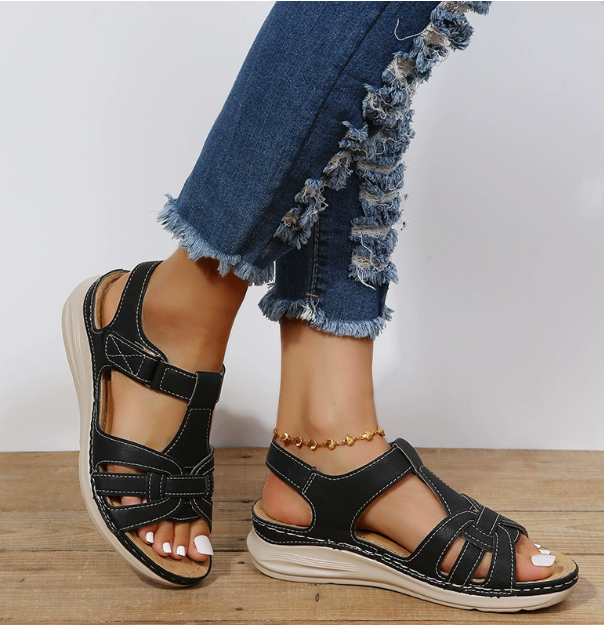Sandales plates femme noires à brides ajourées avec surpiqûres contrastées et fermeture à scratch, semelle épaisse confortable, portées avec jean.