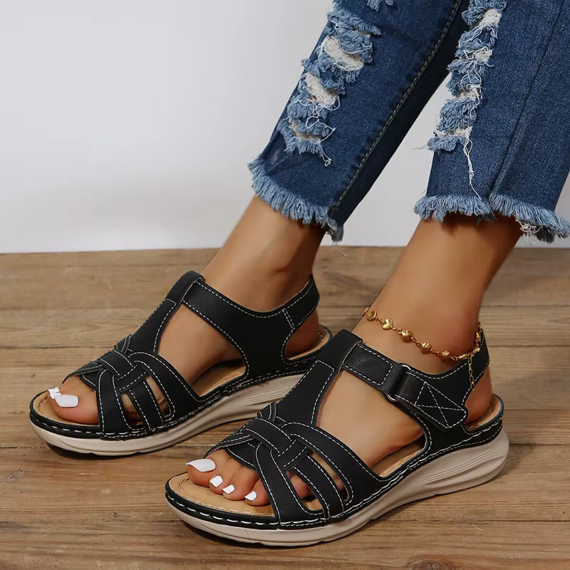 Sandales plates femme noires avec brides croisées, surpiqûres contrastées et fermeture à scratch, semelle confortable, look moderne et pratique.