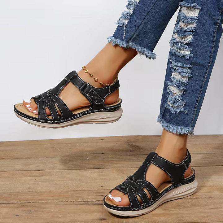 Sandales plates femme noires portées avec jean, brides croisées et fermeture à scratch, semelle épaisse confortable, style moderne au quotidien.