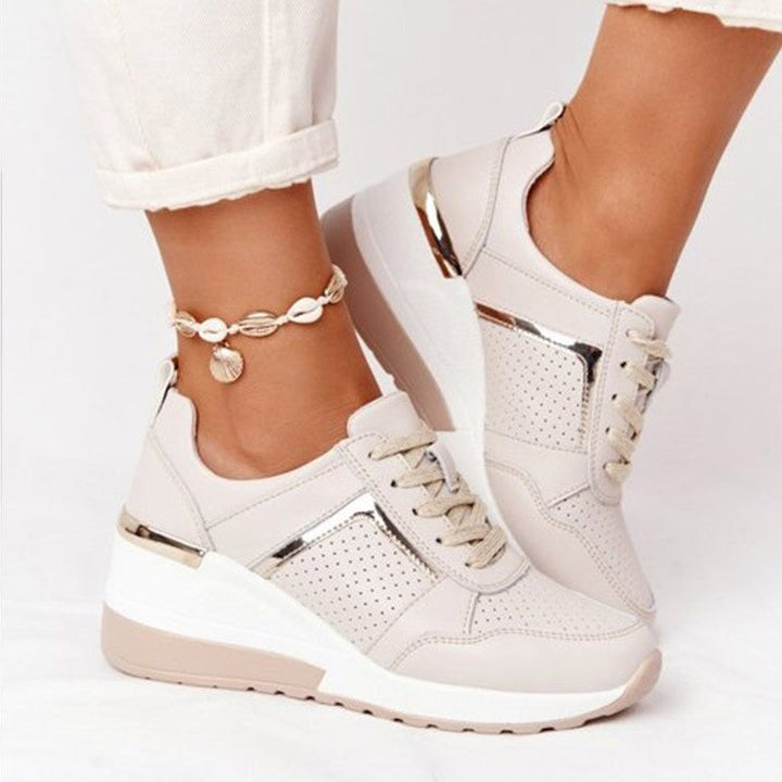 Baskets plates pour femme de couleur beige clair, avec semelle épaisse compensée, détails métalliques argentés et empiècements perforés, portées avec un pantalon clair et un bracelet de cheville, sur fond blanc.