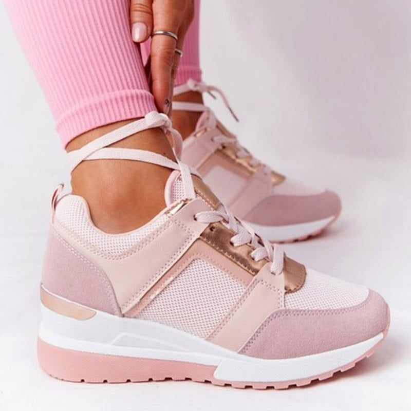 Baskets plates pour femme de couleur rose clair, avec semelle épaisse compensée, empiècements en mesh respirant, détails métalliques dorés et lacets à nouer autour de la cheville, portées avec un legging rose sur fond clair.