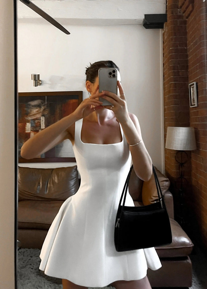 Robe mini femme tendance, idéale pour un look moderne et élégant. Cette robe blanche à décolleté carré et coupe évasée se marie parfaitement avec un sac noir pour un ensemble chic et décontracté. Parfaite pour une sortie en ville ou un événement spécial.